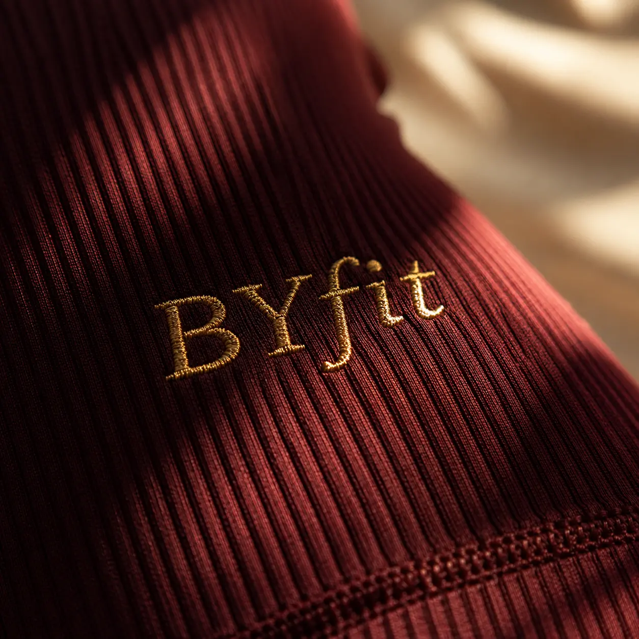 Detalle del bordado dorado BYfit sobre tejido acanalado burgundy